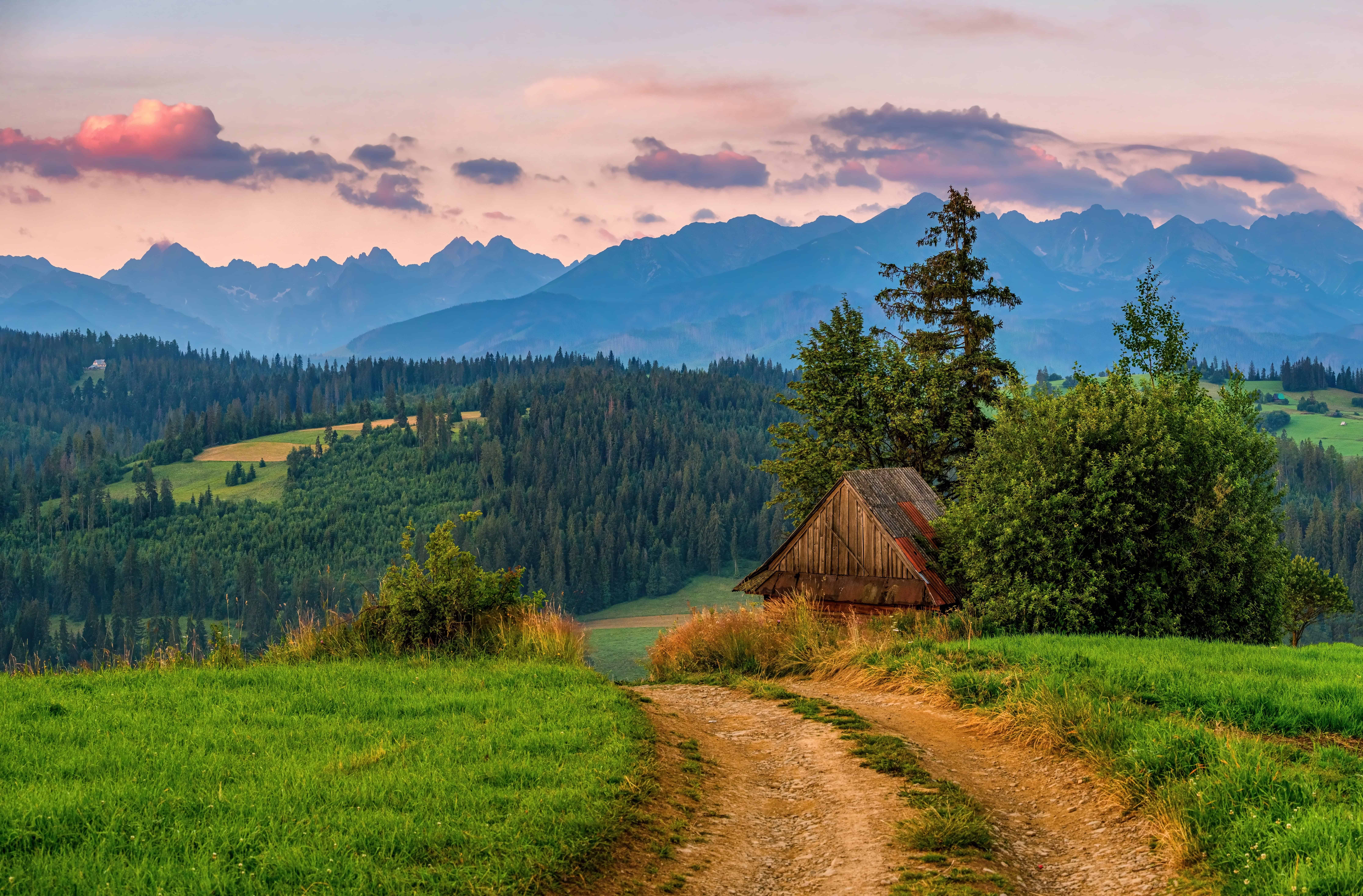 Mountain landscape at sunrise with a dirt road and an old wooden house on a mountain meadow, mountain peaks in the background. Tatra mountain landscape in Poland. Spring nature walks.